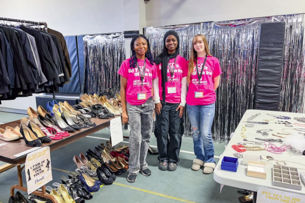 Three volunteers smiling in front of donated shoes